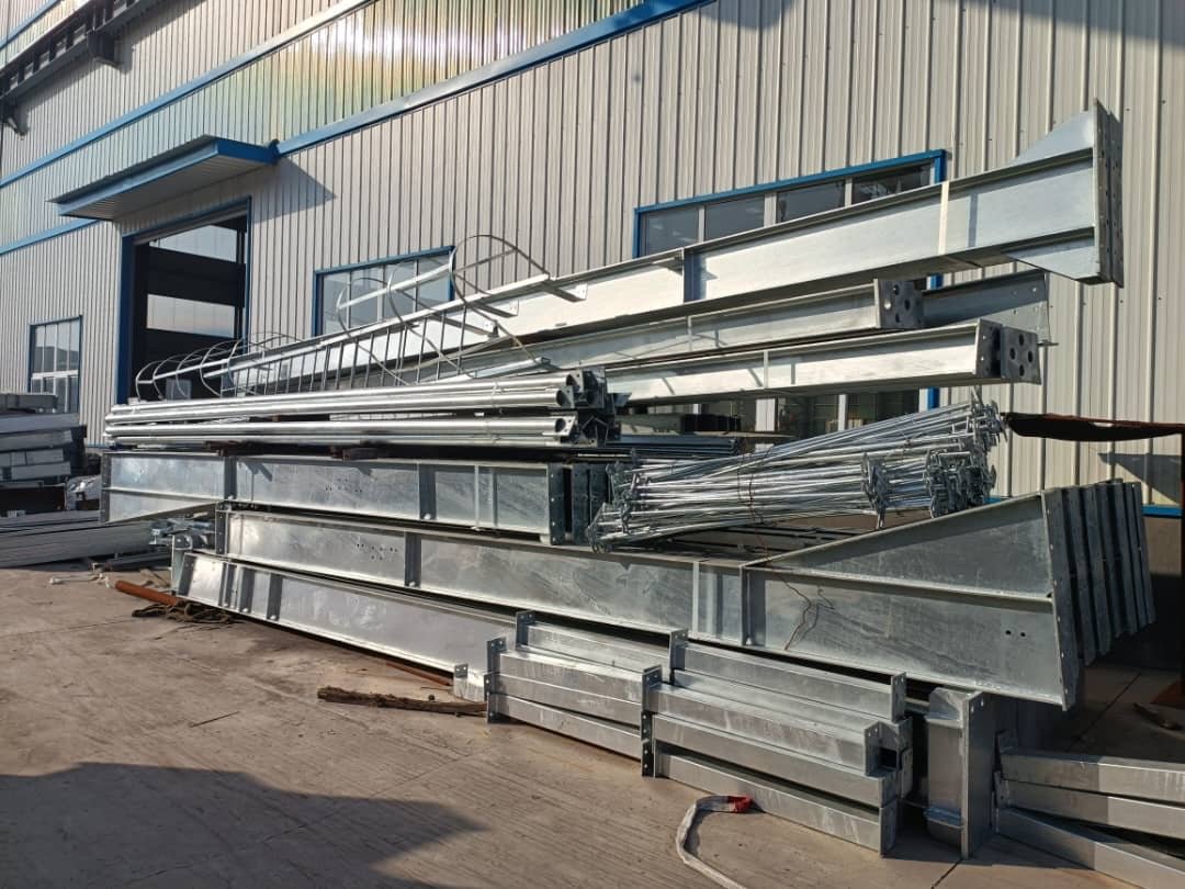 Galvanised steel beams, rods and a caged ladder stacked outside a factory