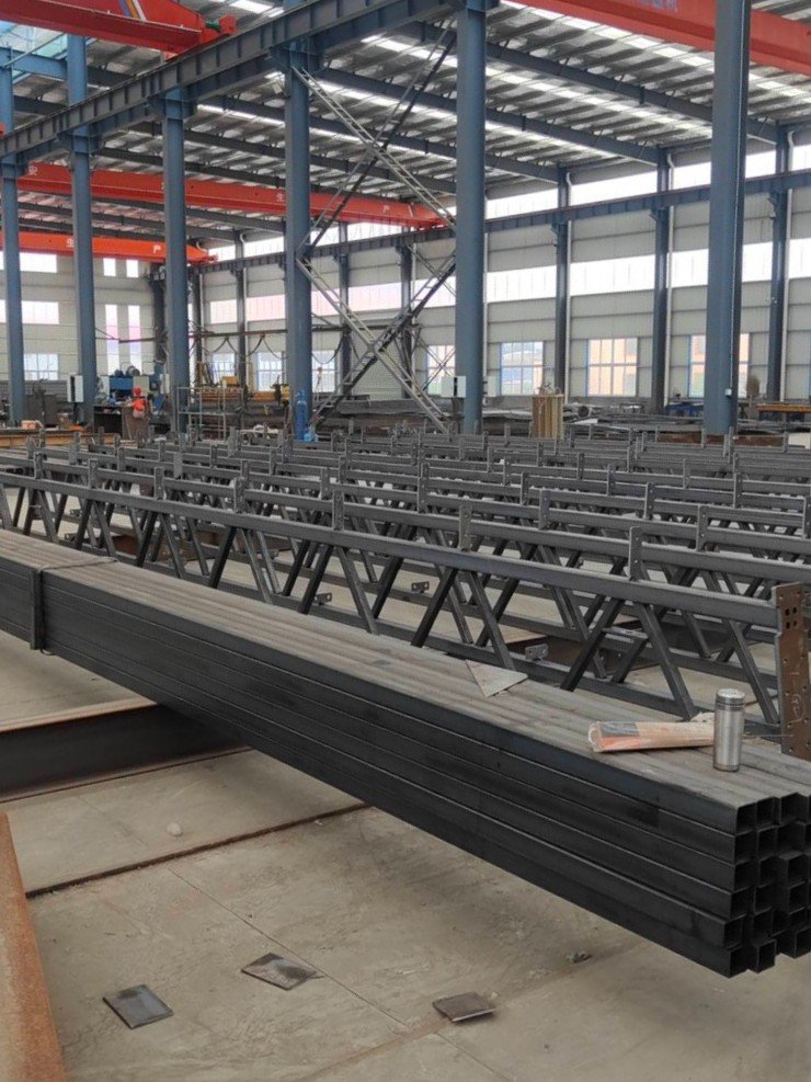 Black steel box sections in front of rows of steel trusses in a factory